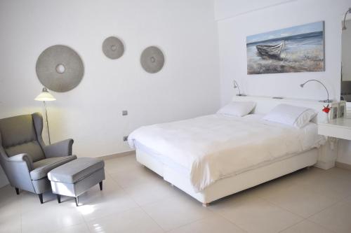 a white bedroom with a bed and a chair at Aegialis Hotel & Spa in Aegiali