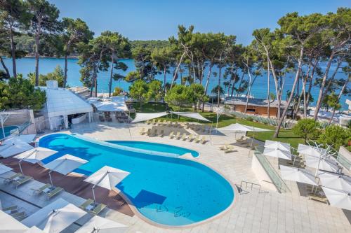 a large swimming pool with umbrellas and the ocean at Hotel Bellevue in Mali Lošinj