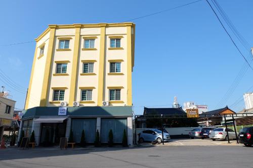 a yellow building with cars parked in a parking lot at Hostel Espace in Chuncheon