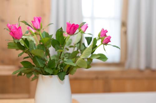 a white vase filled with pink flowers on a table at Garni Bachlerhof in Brunico