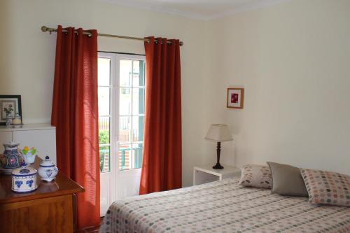 a bedroom with a bed with red curtains and a window at Apartamento de São João in Praia da Areia Branca