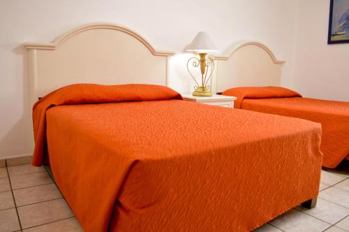 a bedroom with two beds with orange sheets and a lamp at Hotel Costa Brava in Manzanillo