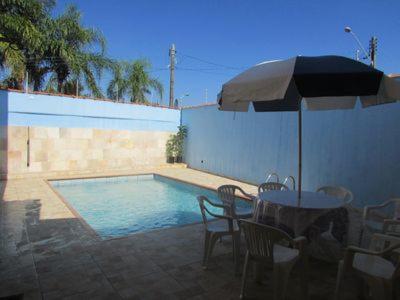einen Tisch mit einem Sonnenschirm und Stühlen neben einem Pool in der Unterkunft Casa c/ Piscina - Ampla e Arejada Balneário Gaivota - 300 mts da Praia in Itanhaém