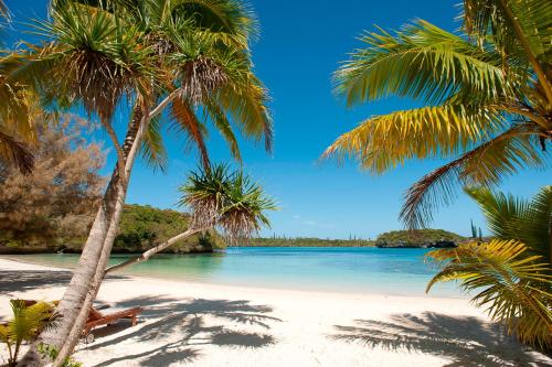 a beach with palm trees and blue water at Oure Lodge Beach Resort in Vao