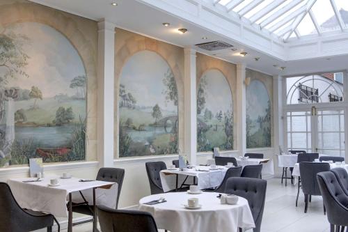 a dining room with tables and chairs and paintings on the walls at Quorn Country Hotel Leicester in Loughborough