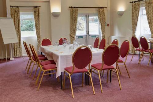 a conference room with a white table and red chairs at The Cedars Hotel in Stowmarket