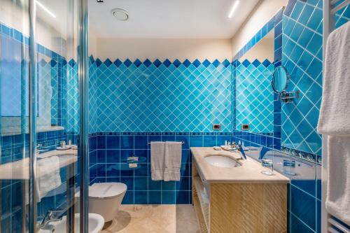 bagno piastrellato blu con servizi igienici e lavandino di Petra Bianca a Porto Cervo