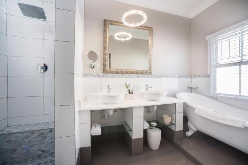 a white bathroom with a tub and two sinks and a bath tub at Batavia Boutique Hotel in Stellenbosch
