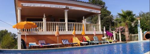 a house with chairs and umbrellas next to a swimming pool at Casa das Oliveiras in Flassans-sur-Issole