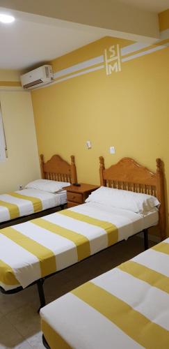 a bedroom with two beds with yellow and white stripes at Pension San Marcos in Alovera