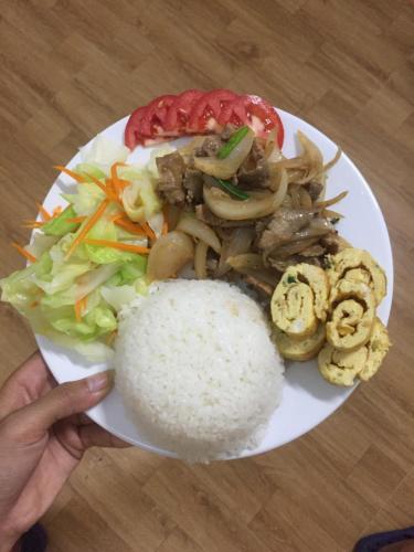 a person holding a plate of food with rice and vegetables at Sunshine Homestay in Phong Nha
