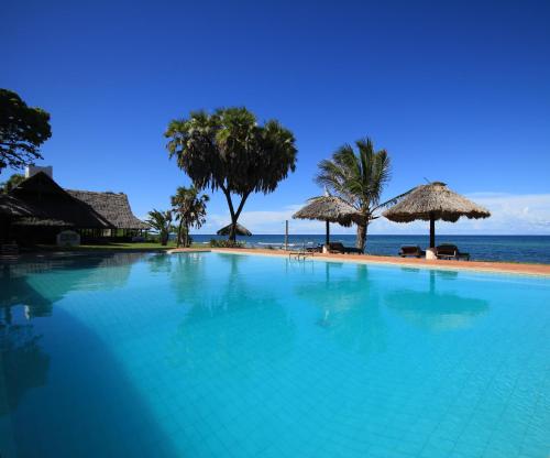 a large swimming pool next to a beach with umbrellas at Amani Beach Resort in Kutani
