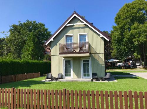 a green house with a balcony and chairs in the yard at Apartment Amber White in Nida