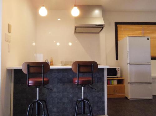 a kitchen with two bar stools and a refrigerator at ウィークリー・マンスリー SORA in Miyako Island