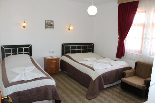 a bedroom with two beds and a chair and a window at Hotel Baykal in Bogazkale