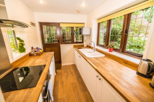 a kitchen with white cabinets and wooden floors and windows at Badgers Den - Covehurst Bay Holiday Cottage in Hastings