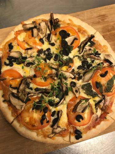 a pizza with tomatoes and mushrooms on a wooden table at Sogn Hotel in Vadheim