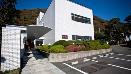 Un bâtiment blanc avec un tas de buissons dans un parking dans l'établissement Shiki Resort Prego Hayama, à Hayama