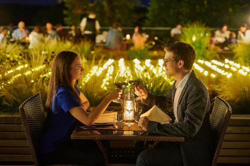 a man and woman sitting at a table with wine glasses at Postojna Cave Hotel Jama in Postojna