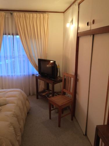 a room with a bed and a tv and a chair at Hostería Bilbao in Villarrica