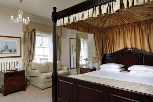 a bedroom with a canopy bed and a chair at Orton Hall Hotel & Spa in Peterborough