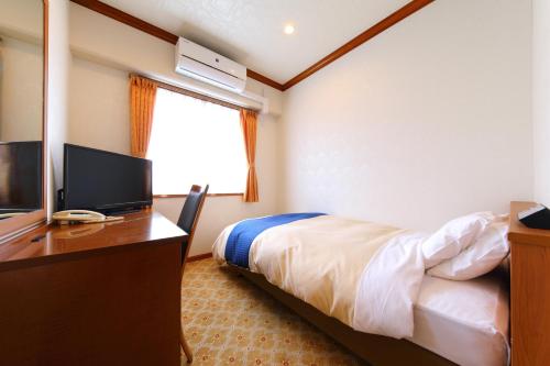 a bedroom with a bed and a desk with a television at Business Hotel Star in Beppu