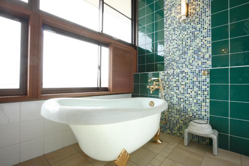 a bathroom with a white tub and green tiles at Hotel Ubudo in Matsushima
