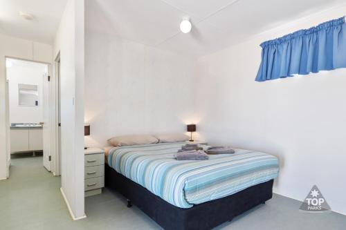 a white bedroom with a bed and a blue curtain at Tasman Holiday Parks - Denham Seaside in Denham