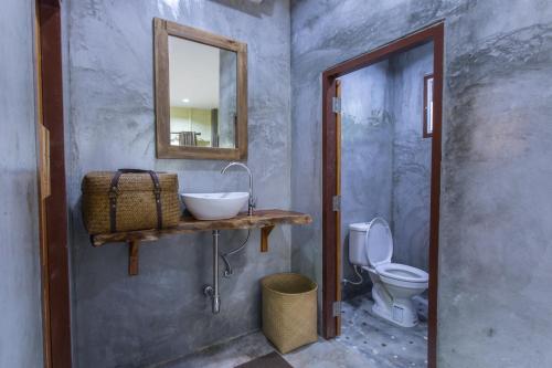 a bathroom with a sink and a mirror and a toilet at P's cottage บ้านพักในสวนสวย in Trang