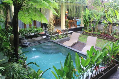 a swimming pool in a garden with two chairs at Donald Home Stay in Ubud