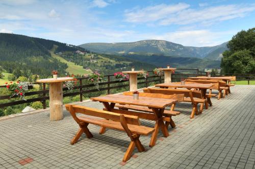 a row of wooden picnic tables with mountains in the background at Horský hotel Žižkova bouda in Pec pod Sněžkou