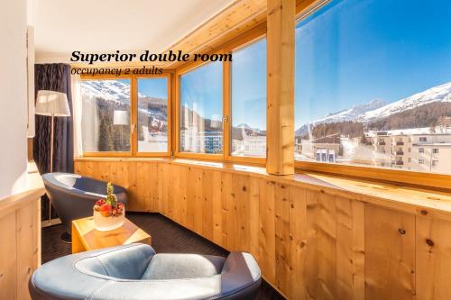 a room with a large window and a blue chair at Hotel San Gian in St. Moritz