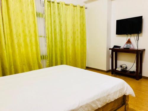 a bedroom with a bed and a tv and yellow curtains at Cedar Peak Condominium in Baguio