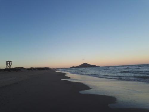 a beach with the ocean and a hill in the distance at Suíte Barros in Navegantes