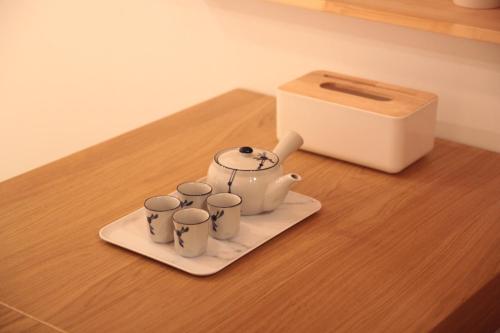 a tea kettle and four cups on a plate next to a box at Lost Circle Homestay in Tainan