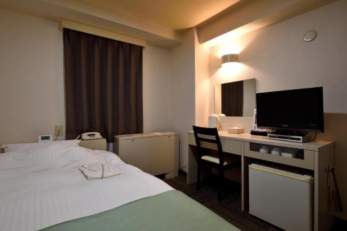仙台市にあるホテル定禅寺のベッド、デスク、テレビが備わるホテルルームです。