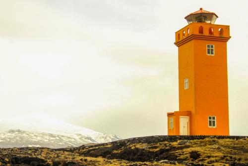 an orange lighthouse sitting on top of a hill at Gotuhus - Ocean View Apartment in Hellissandur