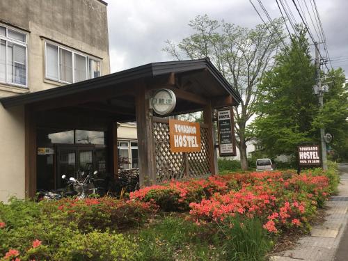 a building with a clock and flowers in front of it at Towadako Hostel in Towada