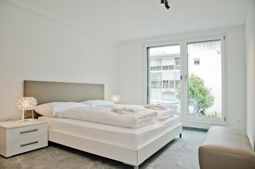 a white bedroom with a large white bed and a window at Apartment JungfrauCenter Brienzersee - GRIWA RENT in Interlaken