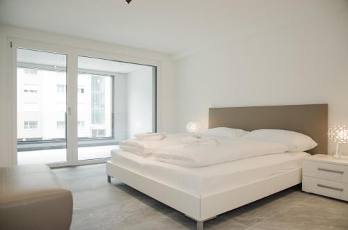 a white bedroom with a white bed and a window at Apartment JungfrauCenter Brienzersee - GRIWA RENT in Interlaken