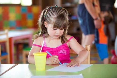a little girl sitting at a table writing on a paper at El Mouradi Club Selima in Port El Kantaoui