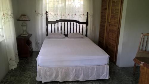 a bedroom with a bed with white sheets and a window at Fairy Hill Palms in Port Antonio