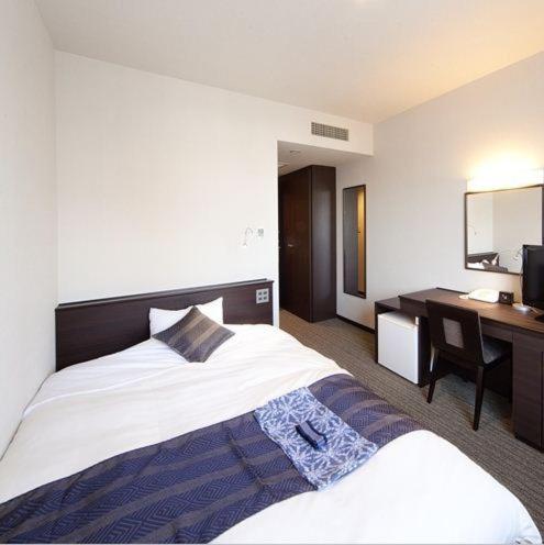 a hotel room with a large bed and a desk at Silk Inn Kagoshima in Kagoshima