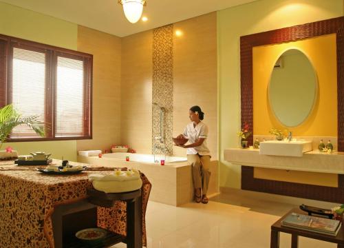 クタにあるザ ラニ ホテル ＆ スパの洗面台2つとバスタブ付きのバスルームに立つ女性