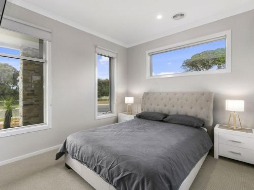a bedroom with a bed and two windows at Bunya By The Sea in Cape Woolamai