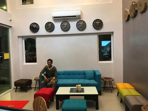 a man sitting on a couch in a room with clocks on the wall at Festival Boutique Hotel - Damai Complex in Kuala Lumpur