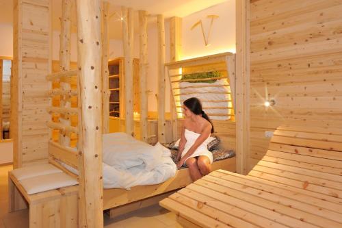 Eine Frau sitzt auf einem Bett in einem Holzzimmer. in der Unterkunft Sieberlechnerhof in Lüsen
