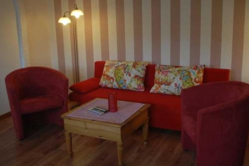 a living room with a red couch and two chairs at Ferienwohnung Nachbars Garten in Grünendeich