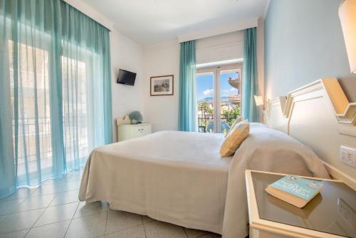 a bedroom with a large white bed with blue curtains at Hotel Ascot Sorrento in Sorrento