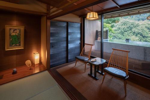 a room with two chairs and a table and a window at Watei Kazekomichi in Atami